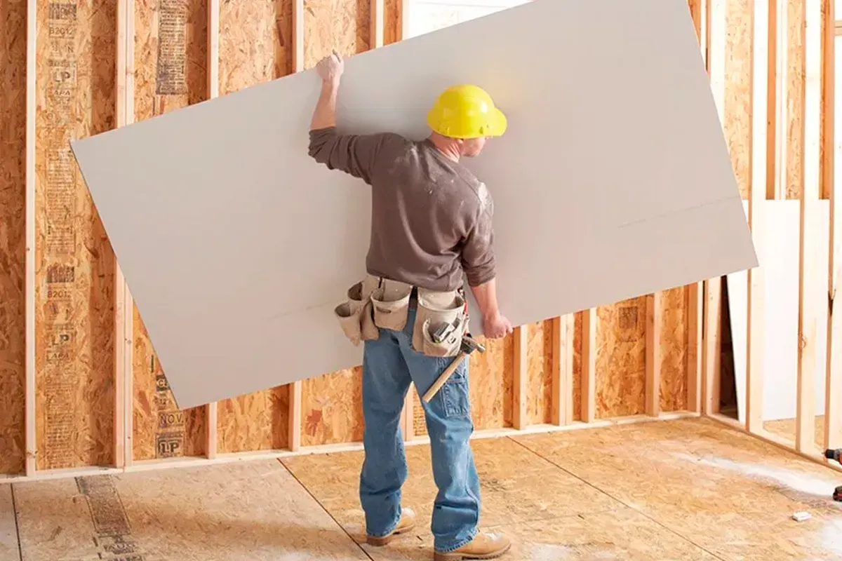 Profissional carregando placa de drywall sobre estrutura de madeira em obra