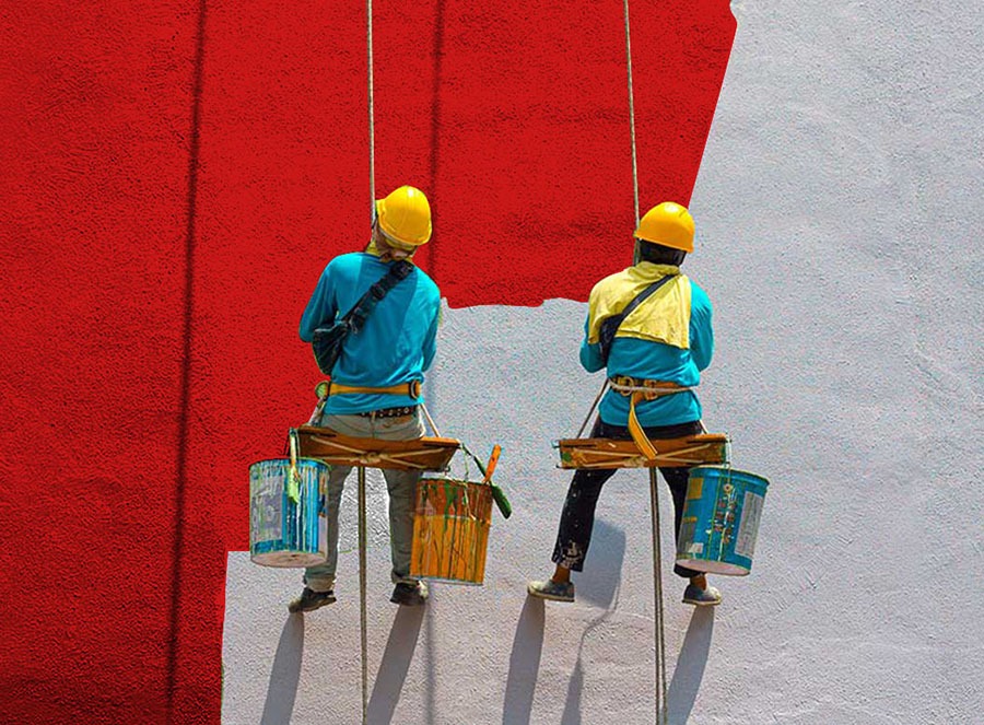 Dois profissionais suspensos em balancim pintando a fachada de um prédio em vermelho e branco